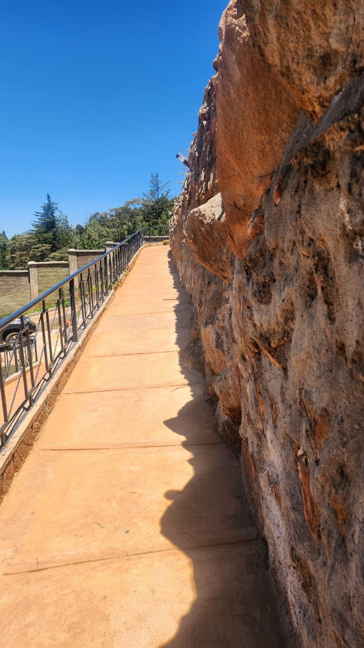 Paved walkway running along the exposed rock face, with a railing overlooking the grounds.