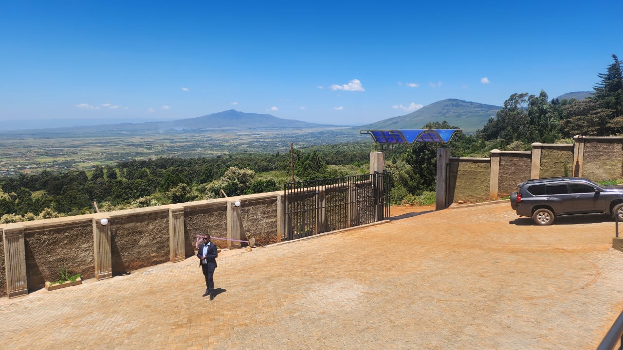 The paved entrance forecourt and gate, looking out across the valley to distant hills.